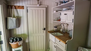 A compact kitchen with white cabinetry, a wooden countertop, and a hanging basket. - Shepherd's hut with hot tub in its own secluded garden (Longtown)