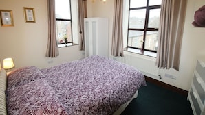 Quarto de hotel com uma cama grande, duas janelas com cortinas, um radiador e um guarda-roupa branco.