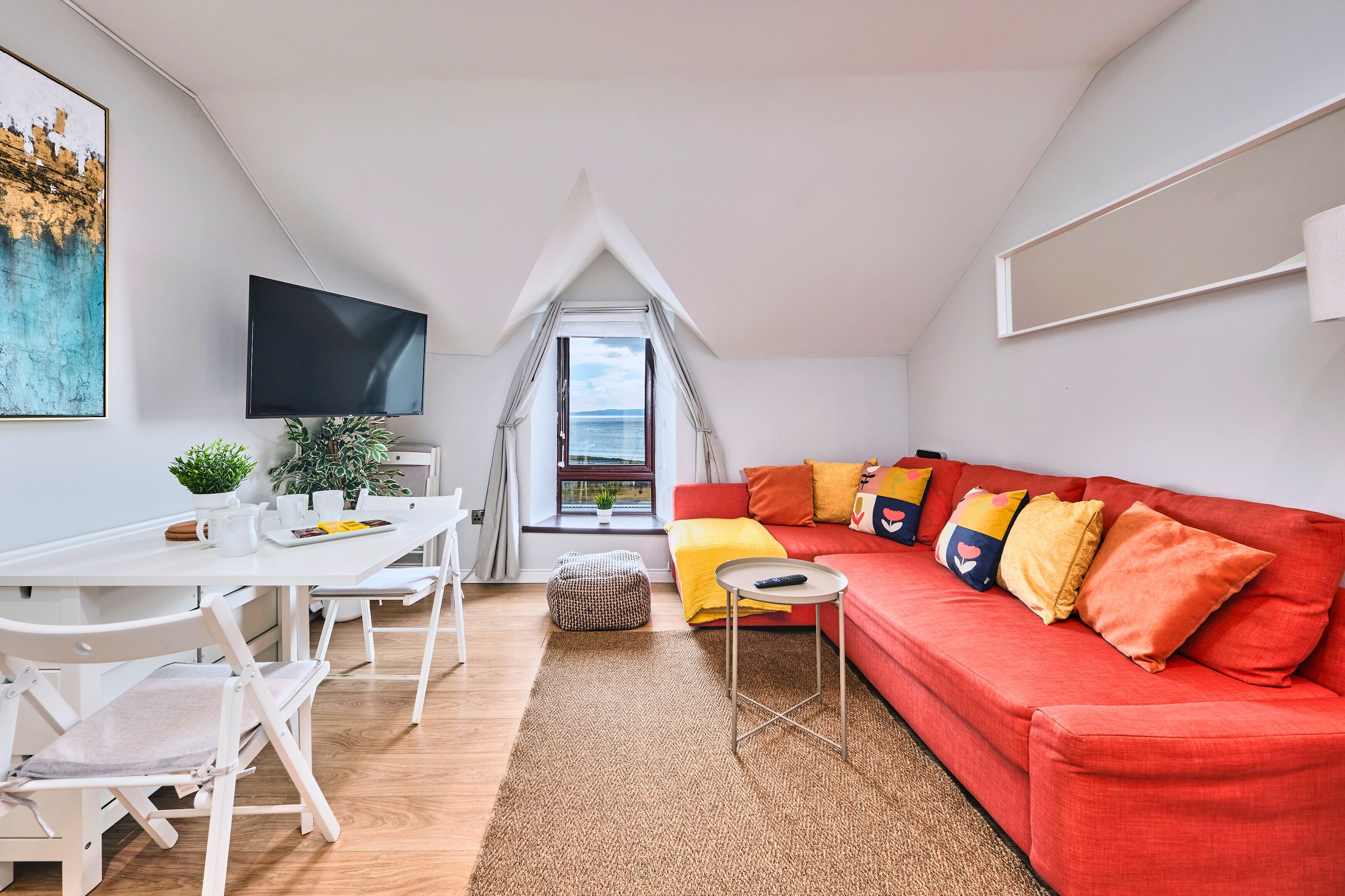 A modern living room with a red sofa, white dining table, and a TV mounted on the wall.