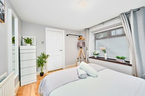 A bedroom with a bed, a dresser, a window with blinds, a lamp, and a plant. - Golf Terrace - Portrush by the Sea (Portrush)