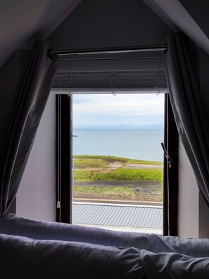 A bedroom with a large window overlooking a grassy landscape and a body of water. - Golf Terrace - Portrush by the Sea (Portrush)