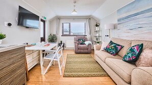 Ett modernt vardagsrum med en soffa, ett soffbord, en tv som är monterad på väggen och ett fönster med persienner.