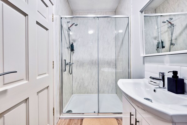 A modern bathroom with a glass-enclosed shower, a white sink with a black soap dispenser, and a mirror above the sink. - Golf Terrace - Portrush by the Sea (Portrush)