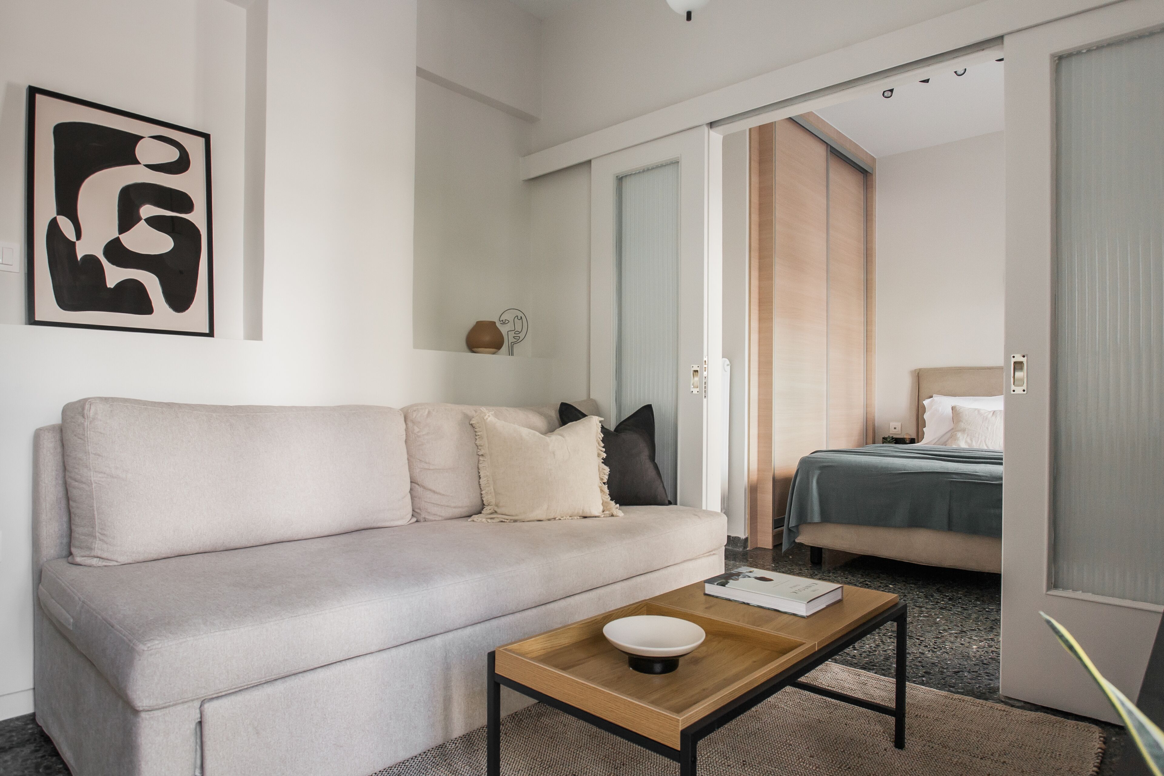 Une chambre d’hôtel moderne équipée d’un canapé, d’une table de chevet, d’un lit et d’une porte donnant sur une autre pièce.