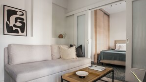 A modern hotel room with a sofa, a bedside table, a bed, and a door leading to another room. - Glorious 1BR Apartment in Athens (Athens)