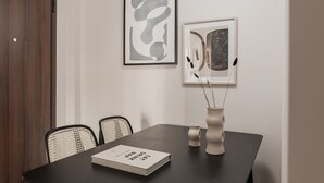 A dining area with a dark wooden table, two framed abstract artworks, a vase with decorative elements, and a book titled "ESTD 2018". - Glorious 1BR Apartment in Athens (Athens)