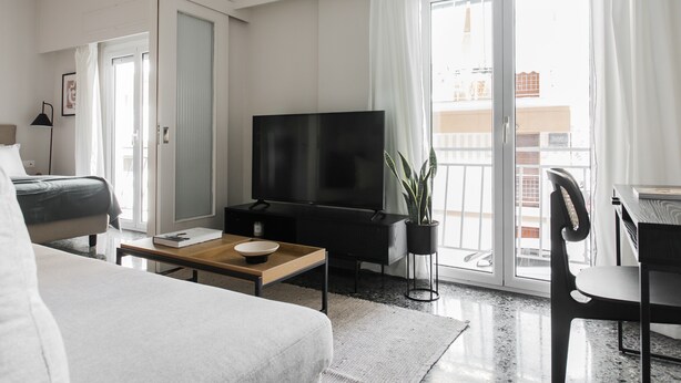 A modern hotel room with a bed, a TV, a dining table, and a balcony with a plant. - Glorious 1BR Apartment in Athens (Athens)