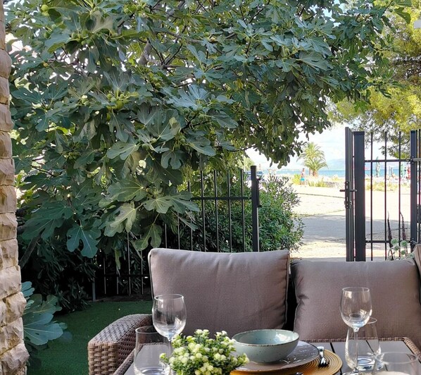 An outdoor seating area with a cushioned bench, a table set with a bowl, wine glasses, and a basket of flowers.