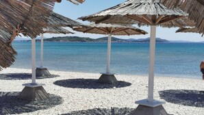 Une plage avec des parasols en chaume et des galets.