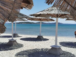 A beach with thatched umbrellas and pebbles.