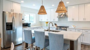 A modern kitchen with white cabinetry, stainless steel appliances, and a central island with bar stools. - Private Pool + STEPS to Beach! LSV/Golf Cart, Bikes, Pet Friendly! Coastal Charmer! (Santa Rosa Beach)
