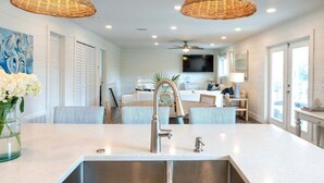 A modern kitchen with a central island, stainless steel sink, and wicker pendant lights. - Private Pool + STEPS to Beach! LSV/Golf Cart, Bikes, Pet Friendly! Coastal Charmer! (Santa Rosa Beach)