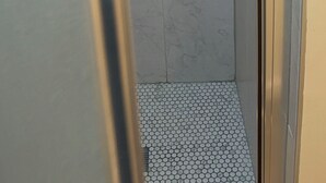 Eine Duschkabine mit Glas, gefliester Boden und eine kleine, geflieste Akzentwand.