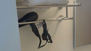 Ein Badezimmer mit Handtuchhalter, gefalteten Handtüchern, einem Fön und einer schwarzen Haarbürste. Über dem Handtuchhalter hängt ein Spiegel, und auf dem Waschtisch stehen zwei Becher.