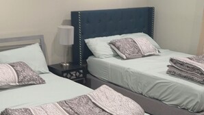 Ein Hotelzimmer mit zwei Betten, jeweils mit Kopfteil, Nachttisch und Lampe. An der Wand hängt ein gerahmtes Bild.