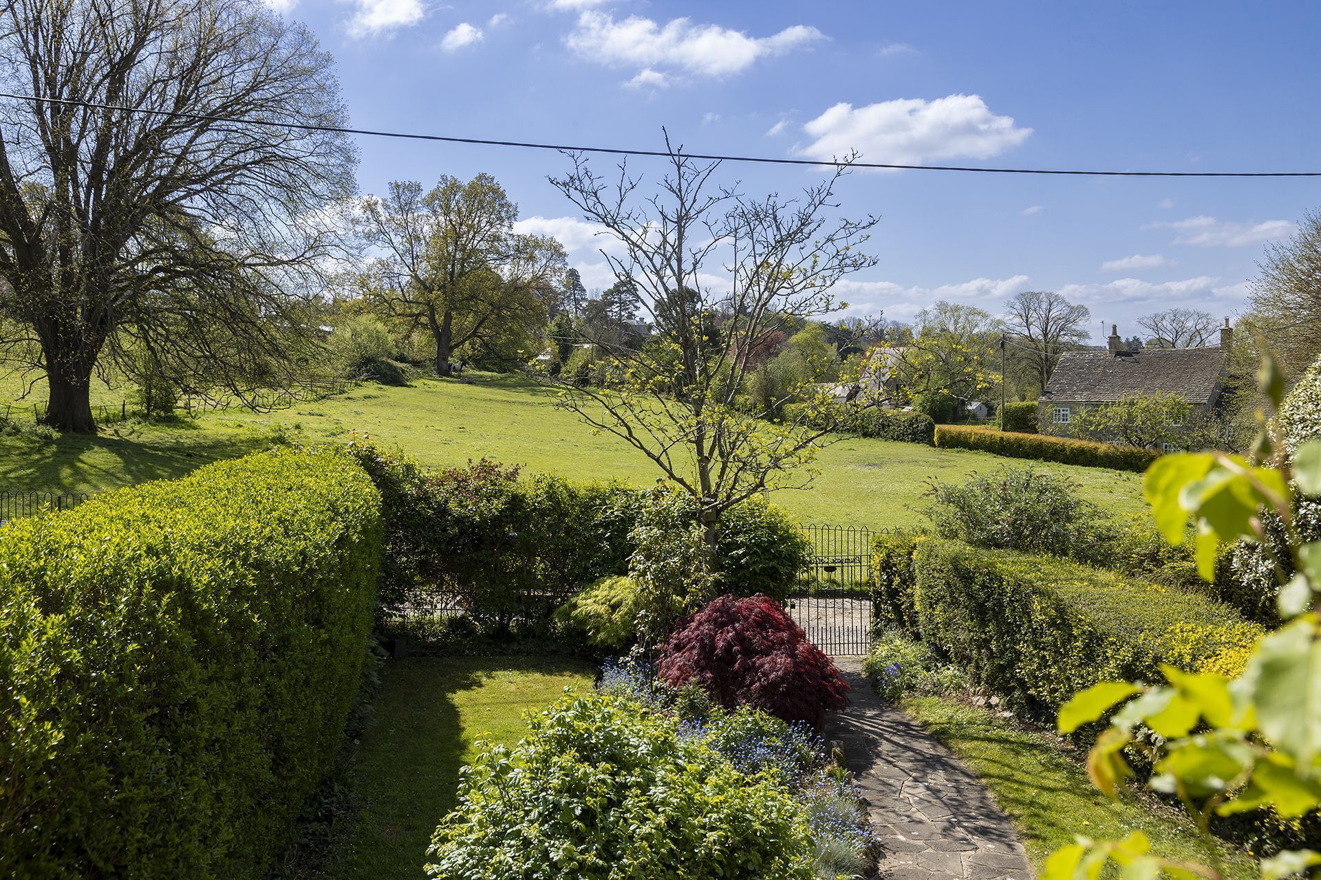 Ein gepflegter Garten mit einem Kiesweg, ordentlich geschnittenen Hecken und verschiedenen Bäumen.