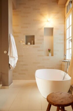 Un baño moderno con una bañera independiente, un taburete pequeño, un perchero y una lámpara de pared.