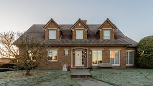 Une maison à deux étages, dotée d’une façade symétrique, d’une entrée centrale et d’un petit porche.