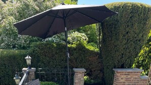 Un espace extérieur aménagé en terrasse, avec des meubles en osier, une table basse en verre et un grand parasol.