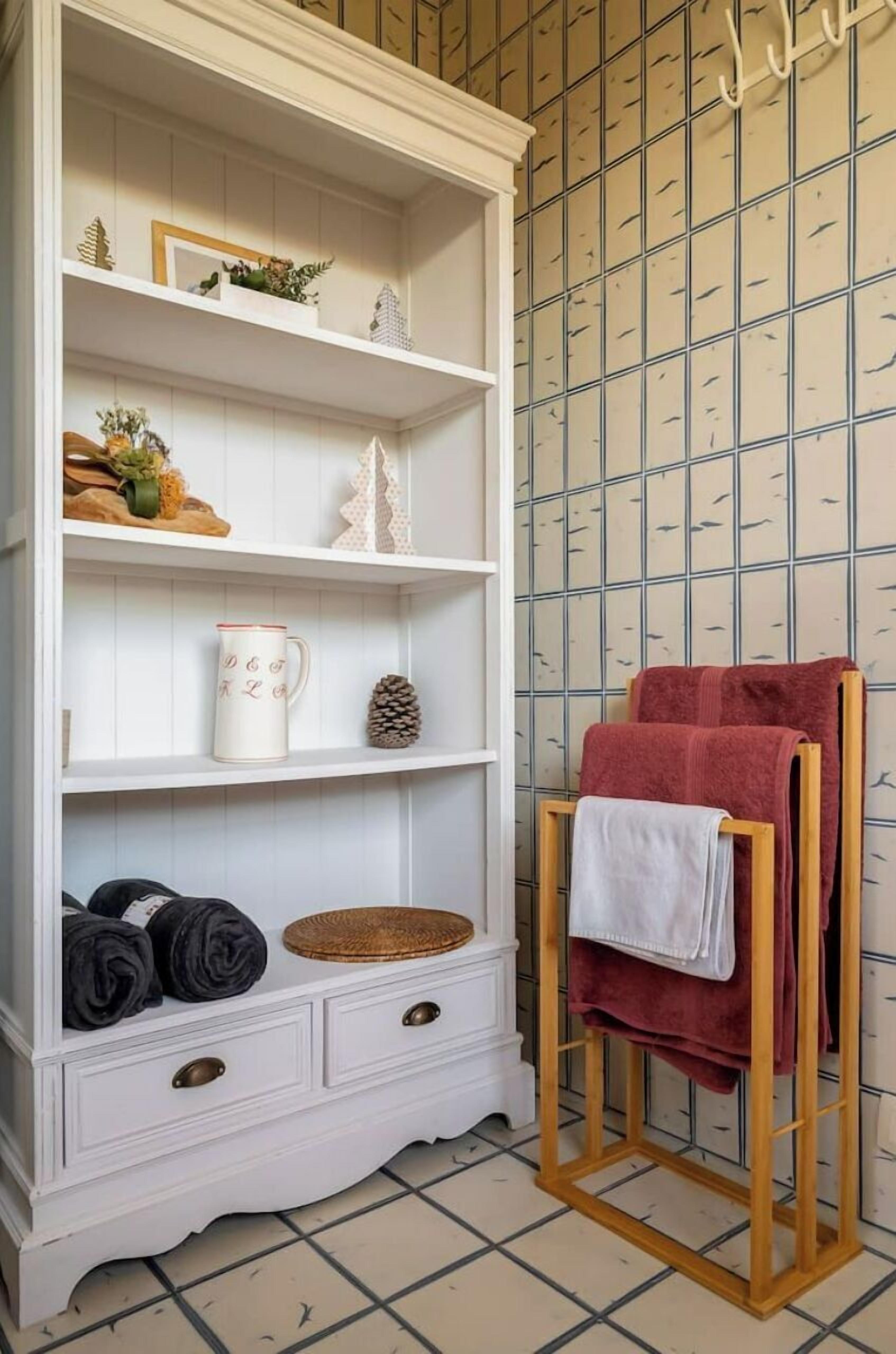 Een witte houten garderobe met meerdere planken en lades, een klein houten krukje met handdoeken, en een betegelde vloer.