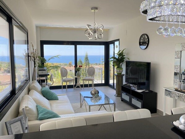 A modern living room with a sofa, TV, and a balcony with a view.