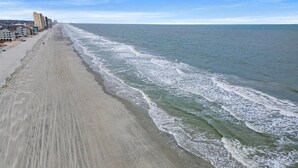 A beach with a long stretch of sand and ocean waves. There are buildings along the shore. - Condo w/ Private Balcony & Stunning Views | Family Friendly (Garden City Beach)