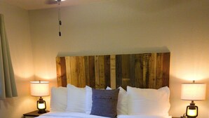 A neatly made bed with white linens and a wooden headboard, flanked by two bedside tables with lamps, in a room with wooden flooring. - Baby Bear Cabin 3 - community pool and hottub. (Branson)