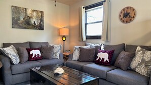 A living room with two grey sofas, a wooden coffee table, a lamp, a painting, and a clock on the wall. - Baby Bear Cabin 3 - community pool and hottub. (Branson)