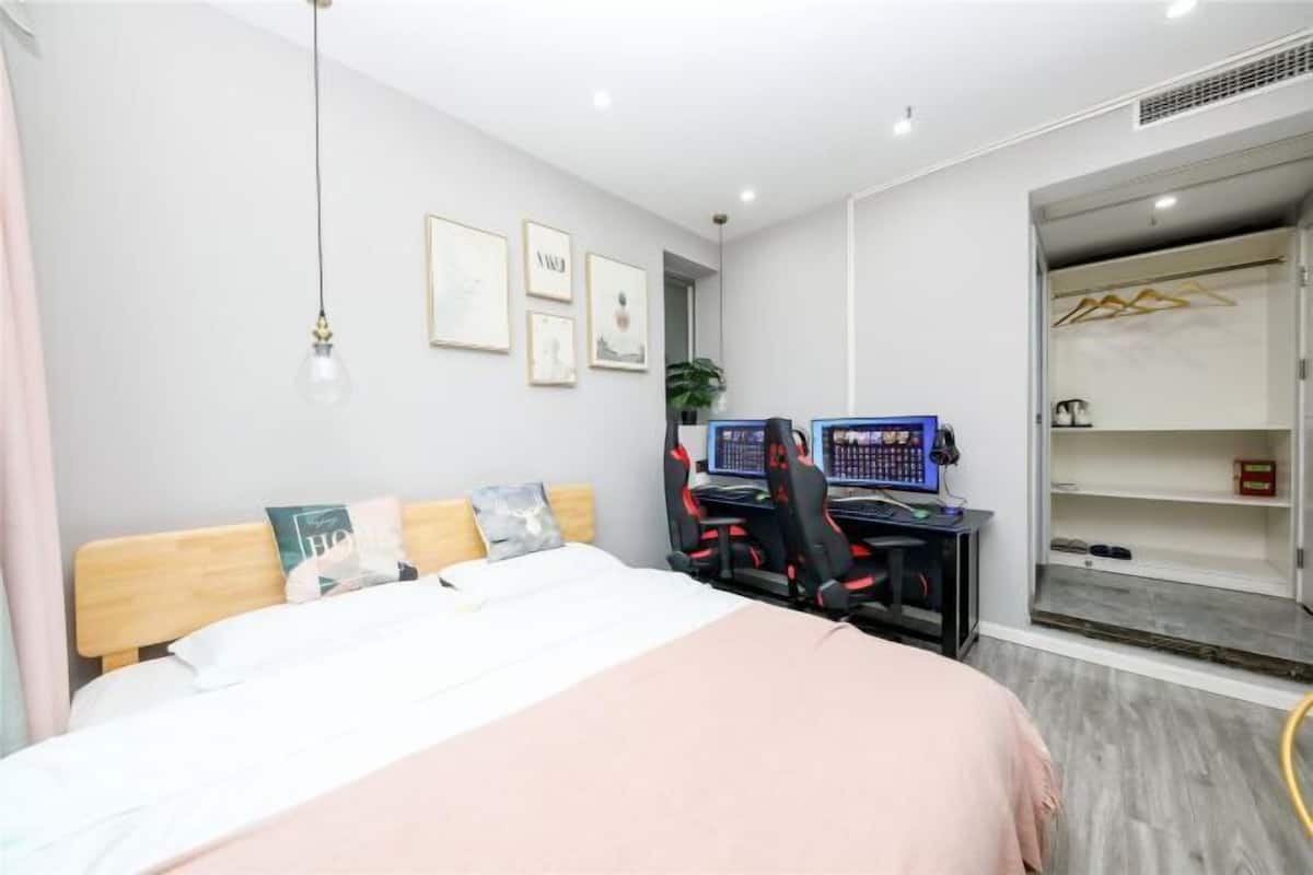 A modern bedroom with a bed, a desk with two monitors, and a walk-in closet.