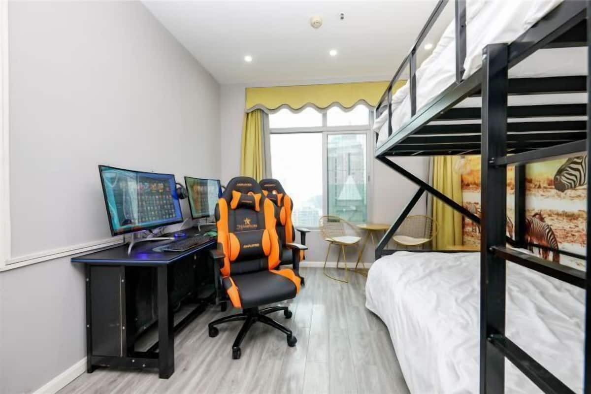 A room with a bunk bed, a desk with two monitors, a gaming chair, and a small table with a chair.