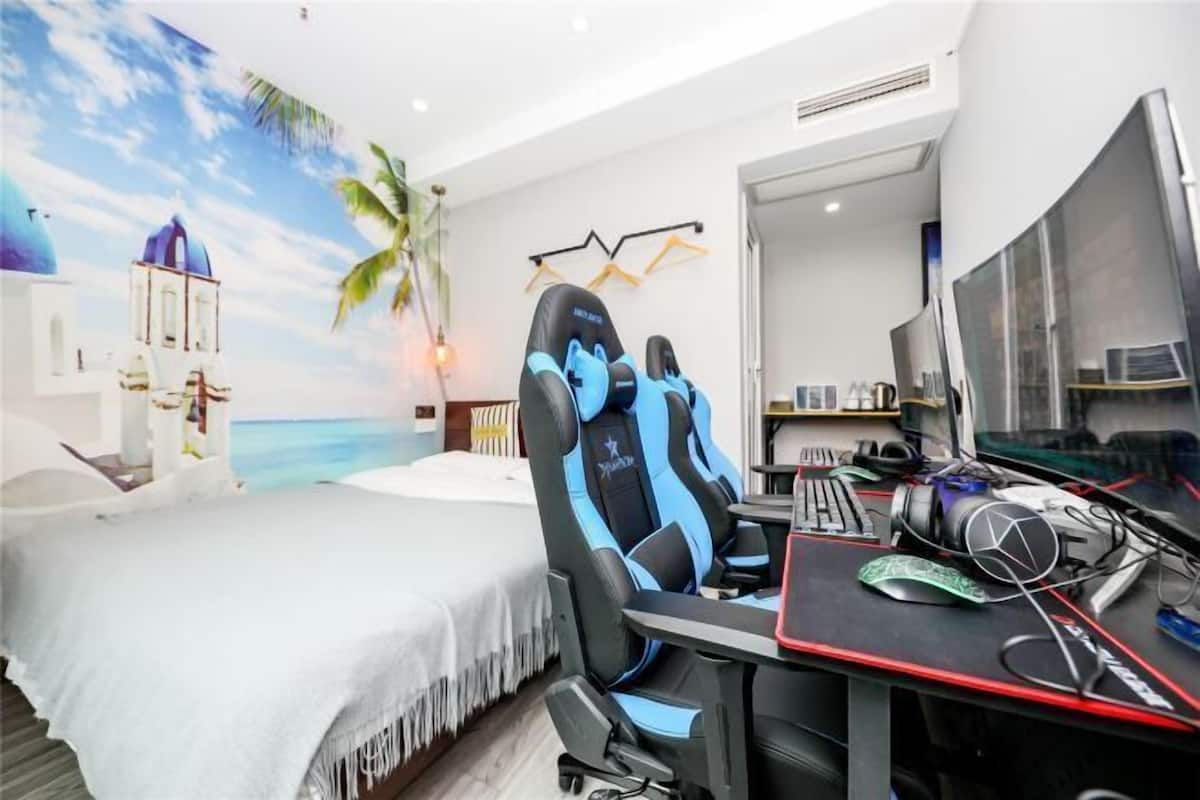 A room with a bed, a gaming chair, a desk with a computer, and a wall mural of a beach scene.