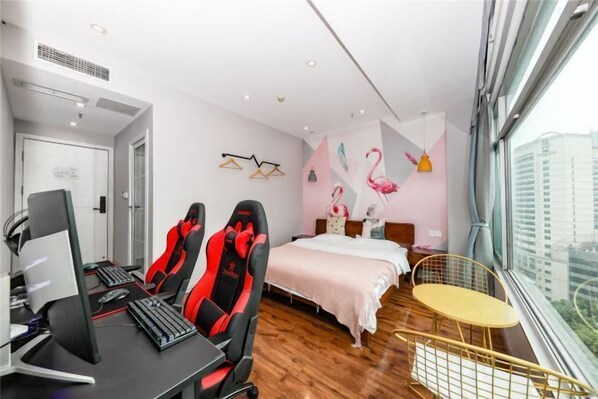 Habitació d'hotel moderna amb escriptori, dues cadires de joc, un llit, taula rodona petita i finestra gran amb vista a la ciutat.