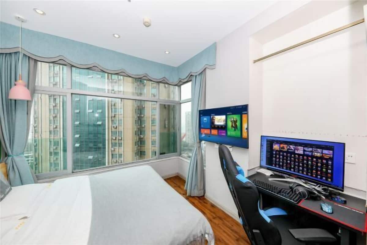 A hotel room with a large window, a bed, a desk with a computer, and a chair.