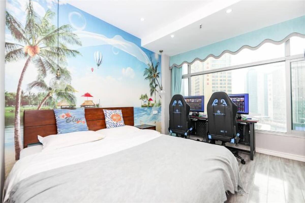 A hotel room with a bed, two monitors, and a large window.