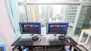 A dual-monitor workstation with a city view, a window with curtains, and a small table.