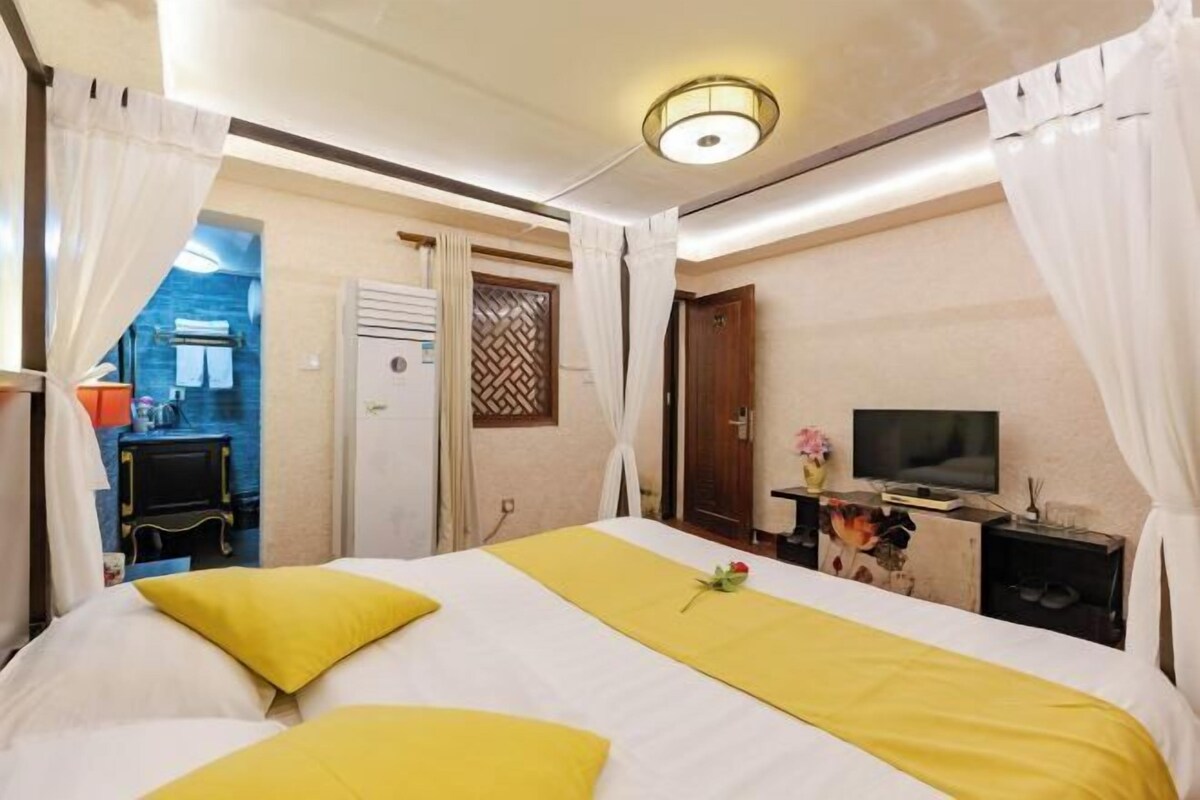 Een hotelkamer met een bed, gordijnen, een televisie en een tafeltje met een bloevas.
