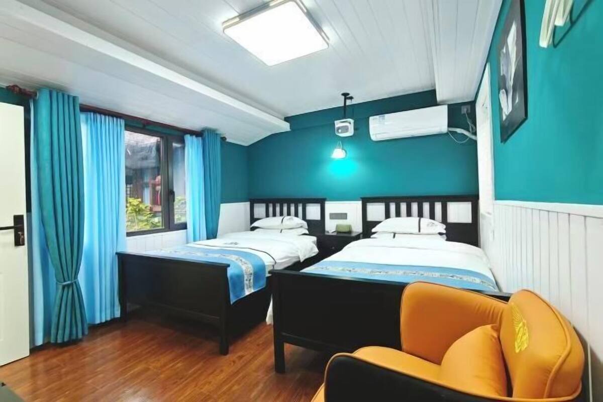 Une chambre avec deux lits, une chaise, une fenêtre avec des rideaux, un luminaire au plafond et un appareil de climatisation.