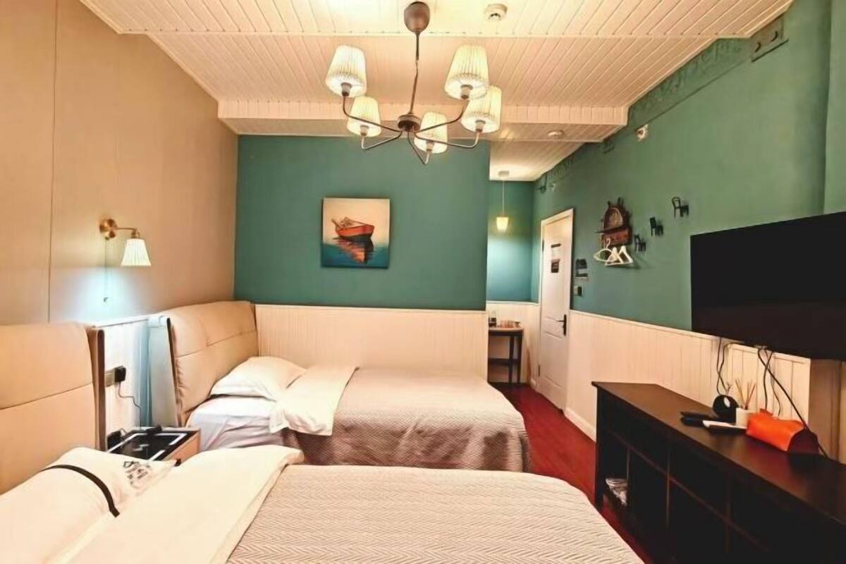 Une chambre avec deux lits, une télévision, un bureau et un tableau au mur.