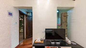 A modern living room with a flat-screen TV on a black stand, a small table with decorative items, and a stone accent wall.