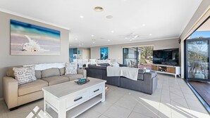 Un salon moderne avec un canapé, une table basse et un téléviseur. On y trouve également un coin repas avec des chaises et une table. La pièce est dotée de grandes fenêtres et offre une vue sur l’extérieur.