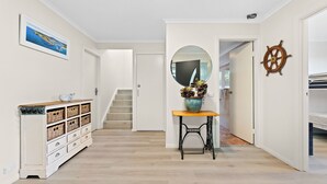 Un couloir avec un escalier, une commode blanche avec des paniers, un miroir et un élément de décoration représentant un gouvernail de bateau.