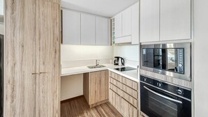 A modern kitchen with white cabinets, a wooden cabinet, a built-in oven, and a coffee maker. - Miramar Deluxe con Vista al Mar (Concón)