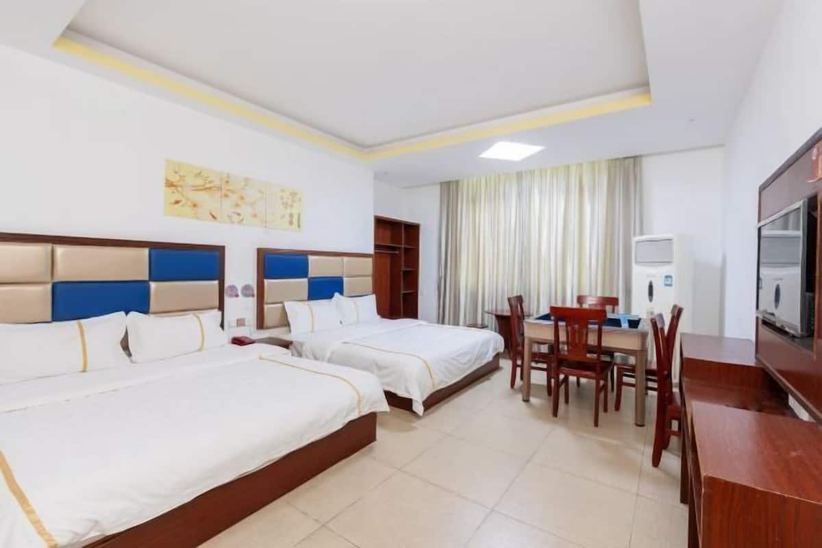 A hotel room with two beds, a dining table, chairs, a TV, and a window with curtains.