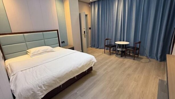 A hotel room with a bed, a small table with chairs, a door, and a curtain.