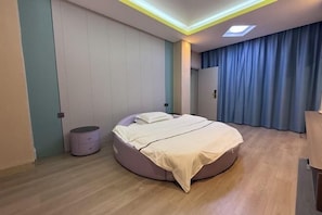 A modern bedroom with a round bed, a small bedside table, a wardrobe, and a ceiling light fixture. - Danzhou Hongyunting Hotel (Danzhou)