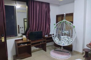A room with a television on a wooden stand, a hanging chair, a desk with a computer, and a window with curtains. - Danzhou Hongyunting Hotel (Danzhou)