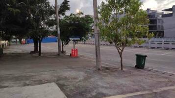 Un espacio pavimentado con árboles, un contenedor de basura y una valla.