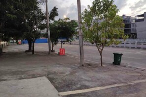 Une zone pavée avec des arbres, une poubelle et une clôture.