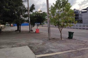 Un espacio pavimentado con árboles, un contenedor de basura y una valla.