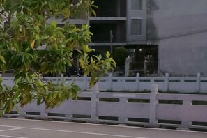 A building with a white fence, a tree with green leaves, and a paved area. - Danzhou Hongyunting Hotel (Danzhou)